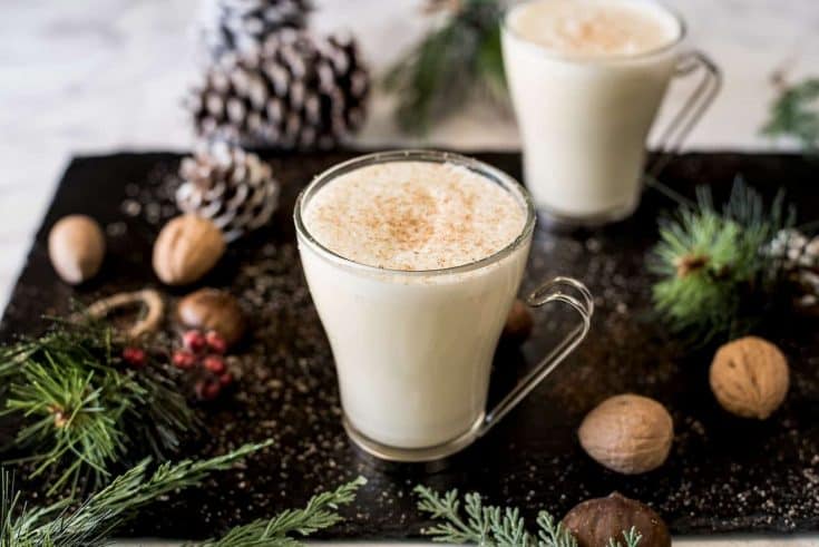 Eggnog in glass mugs surrounded by shelled nuts, pine cones and fern