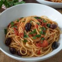 Shiny black olives, tomato and parsley with spaghetti in a white bowl