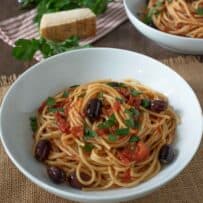 A bowl of spagehetti with tomato sauce, olives and capers