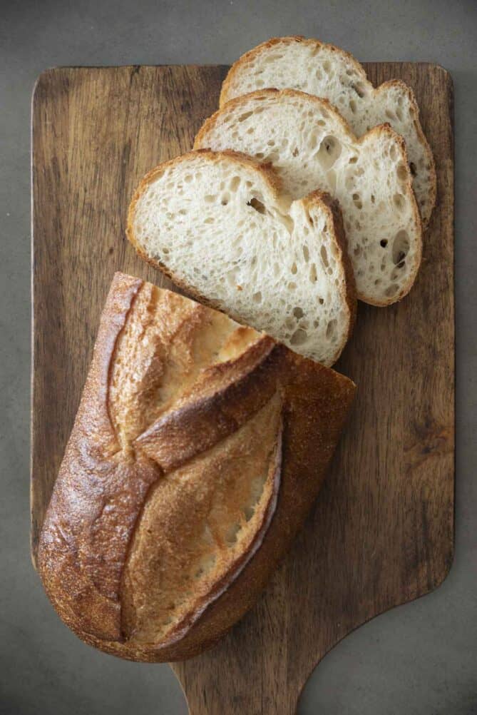 A loaf of crusty bread with slices on a cutting board
