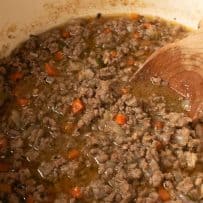 A closeup of white Bolognese sauce cooking in a pan with chopped carrots