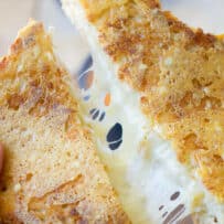 A grilled cheese made with 3 cheeses cut in half and being pulled.