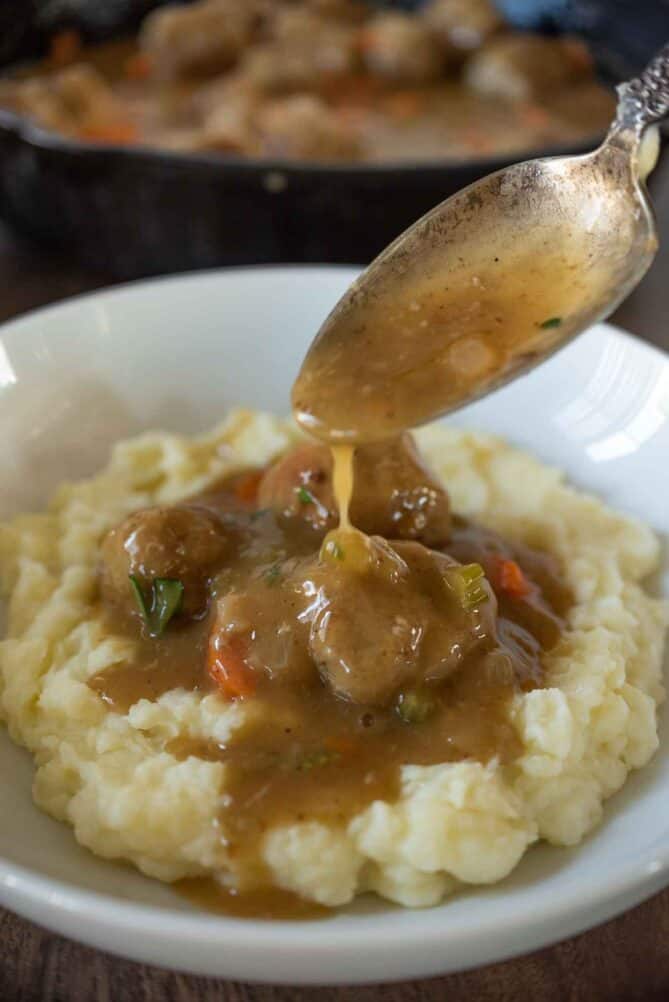 Using a spoon to pour gravy over meatballs
