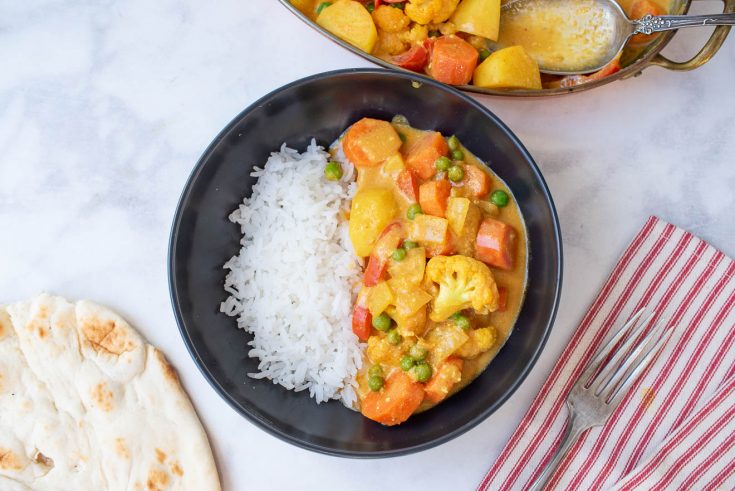 A black bowl filled with white rice and vegetable curry