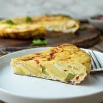 A slice of Spanish omelette on a plate viewed from the side showing the colorful vegetables inside