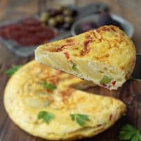 Lifting a slice of Spanish tortilla showing the potato slices, red pepper and green zucchini/courgette on the inside