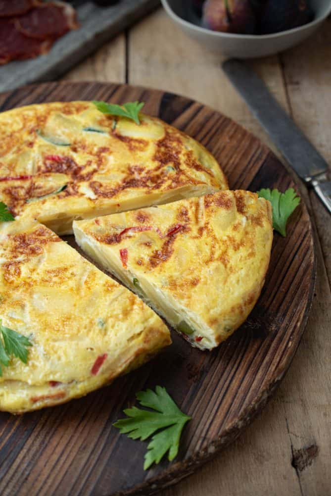 A whole Spanish omelette/tortilla on a round wood board with a triangular slice cut