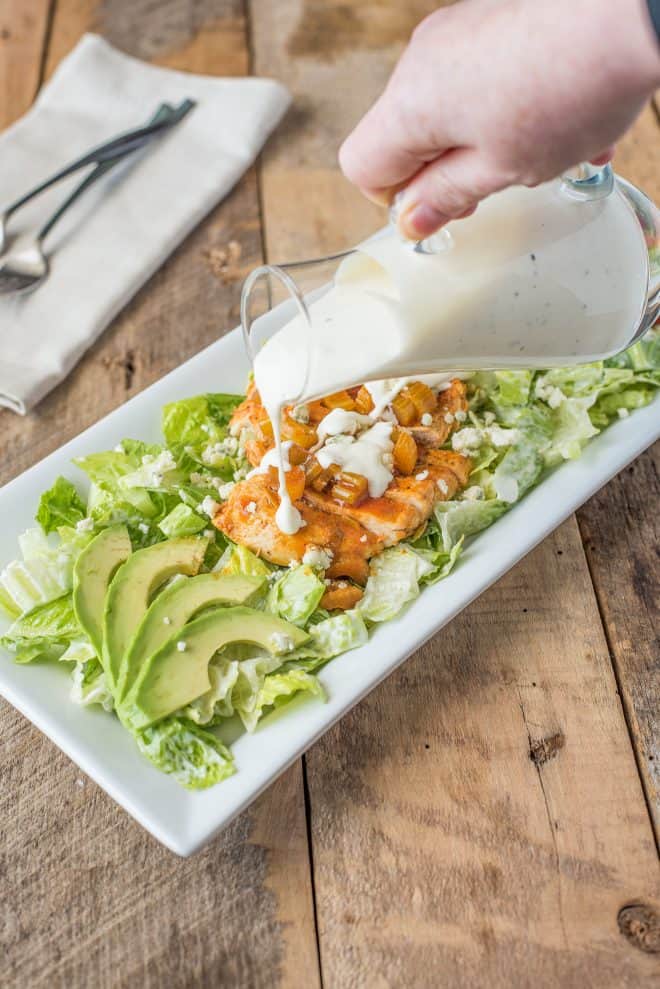 Pouring blue cheese dressing over buffalo chicken salad
