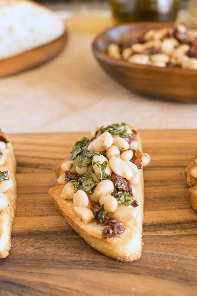 A closeup of a Tuscan bean crostini topped with crispy kale