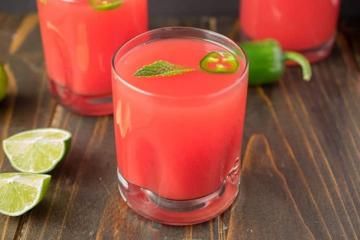 A vibrant watermelon colored drink with green mint and jalape&ntilde;o slice floating on top