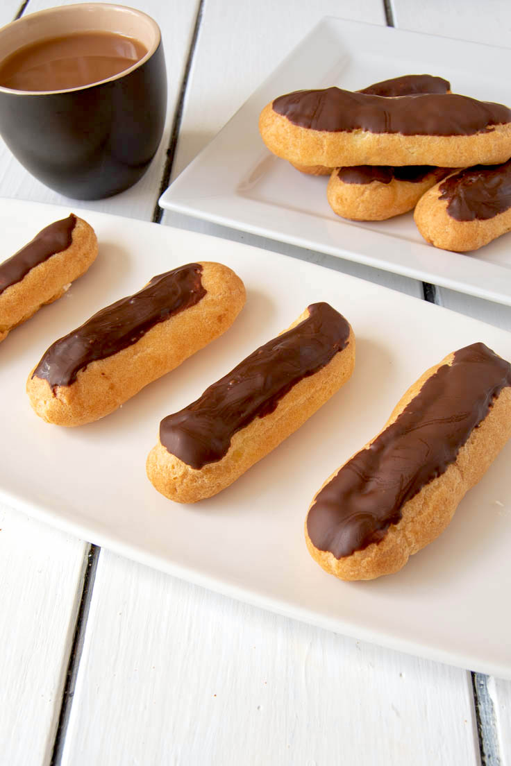 Whipped cream chocolate eclairs on a white plate with a cup of coffee