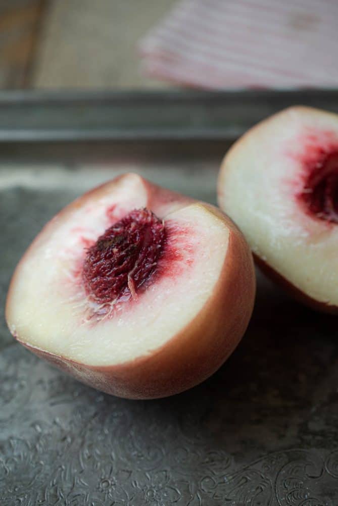 A white peach cut in half showing the white flesh with a red center and pit.