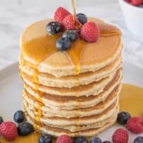A large stack of pancakes topped with fruit pouring over syrup