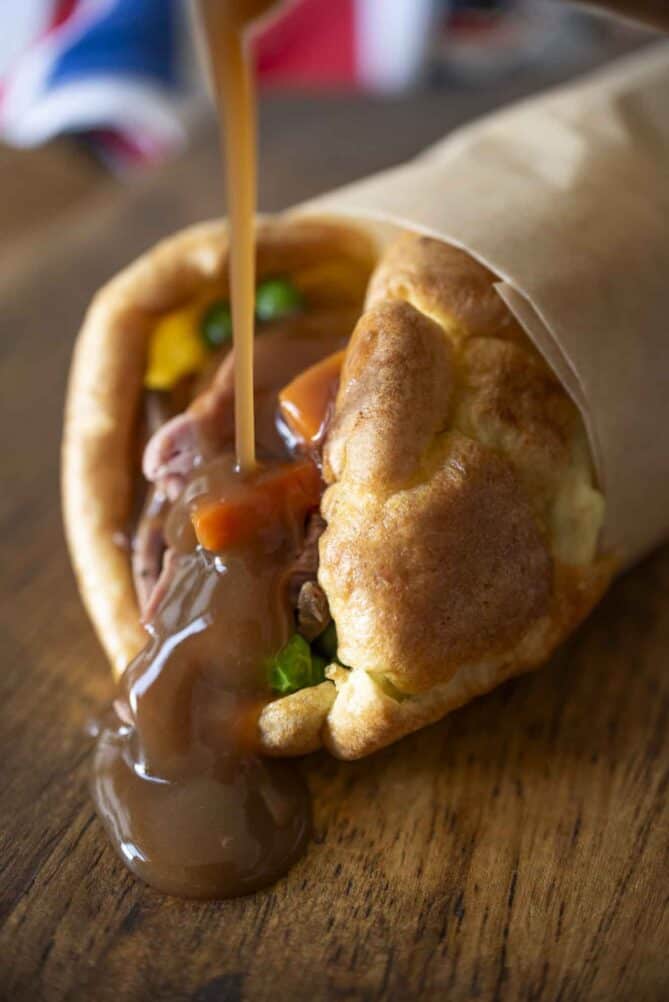 Pouring gravy over roast beef and vegetables wrapped in a Yorkshire pudding