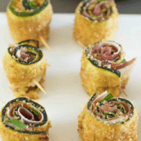 A closeup of breaded zucchini rolled up and secured with toothpicks