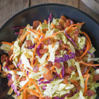 A black bowl filled with coleslaw with bacon pieces in a no-mayo vinaigrette.